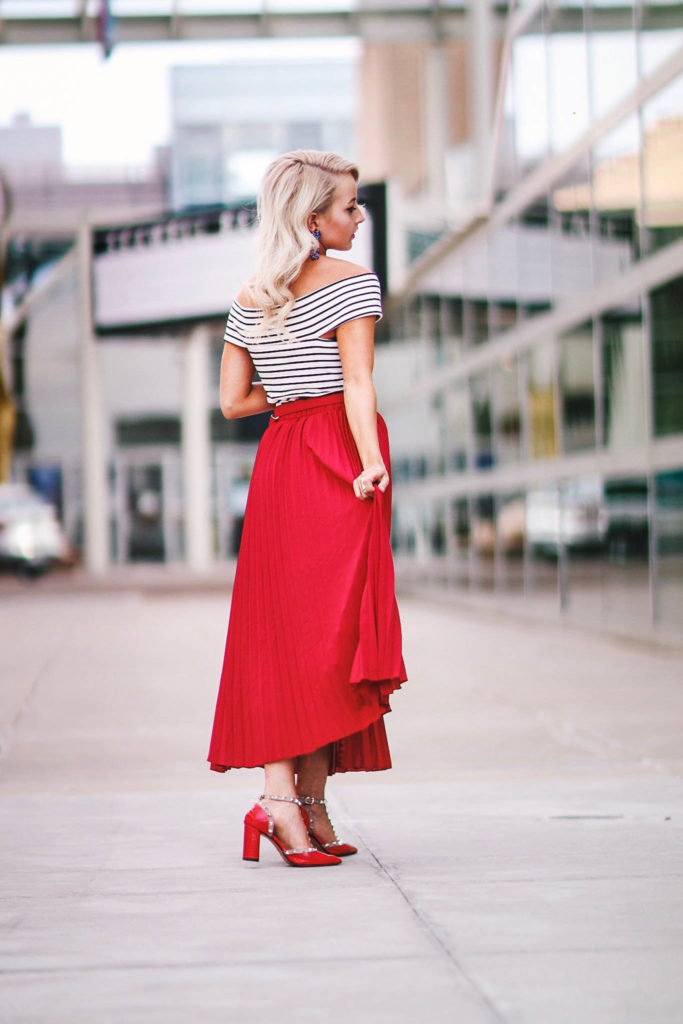 Alena Gidenko of modaprints.com styles a red pleated skirt with an off shoulder stripped top and studded Valentino heels