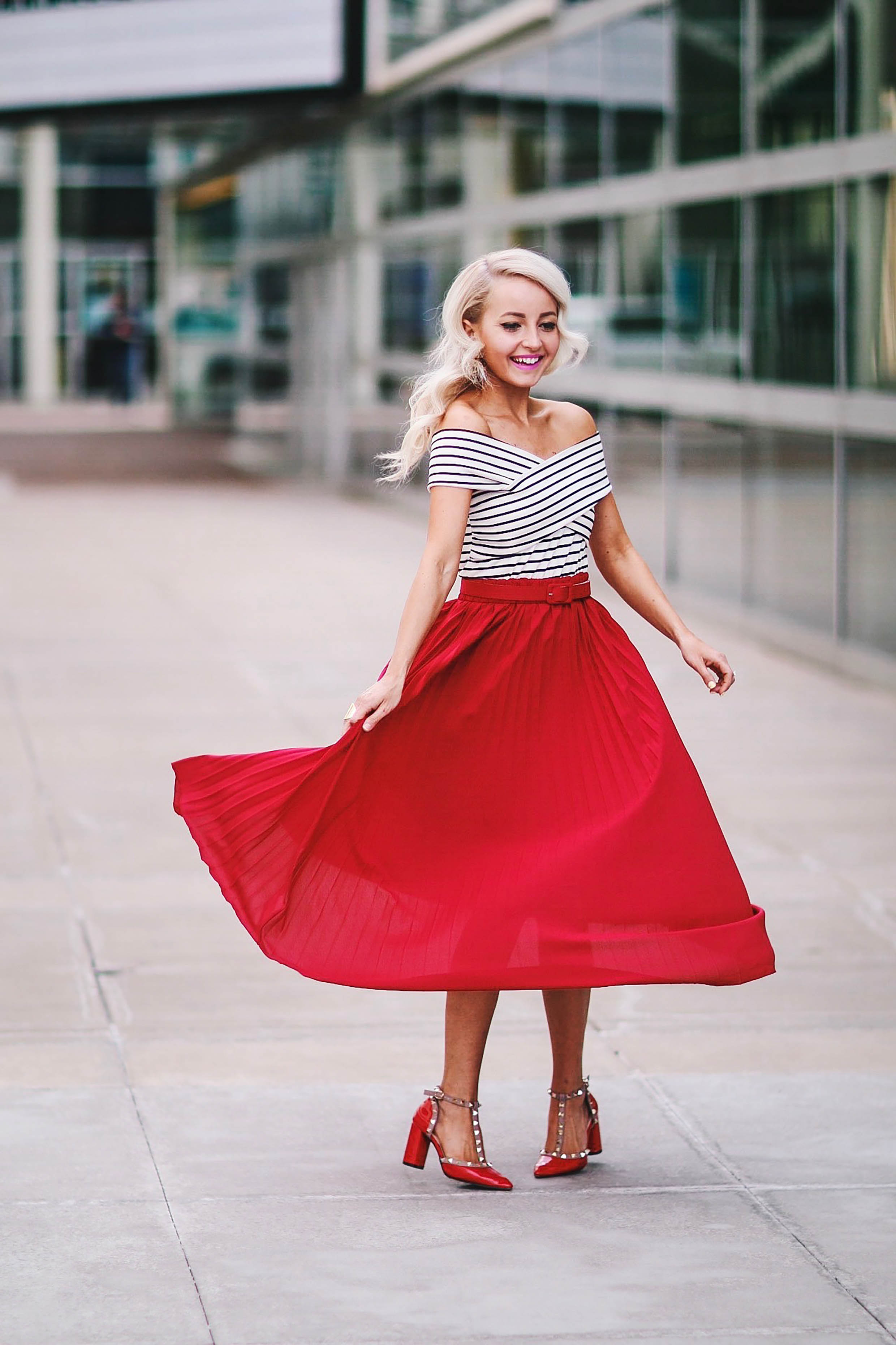 Alena Gidenko of modaprints.com styles a red pleated skirt with an off shoulder stripped top and studded Valentino heels